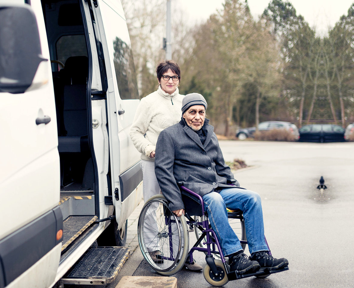 woman assisting senior man on wheelchair in exiting van